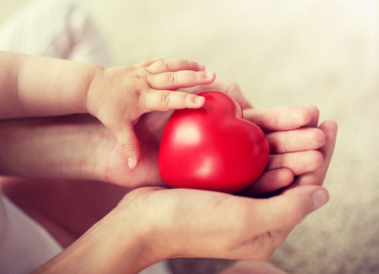 close up of baby and mother hands with red heart
